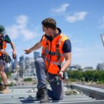 Construction workers wearing safety gear are on a rooftop.